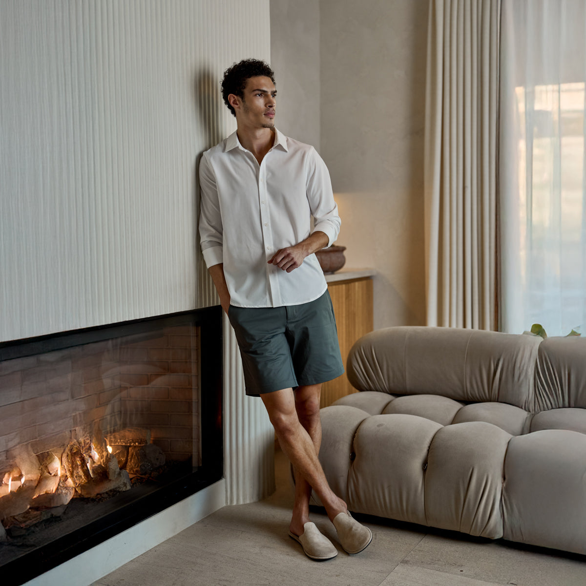 Man in a white shirt and shorts beside a fireplace