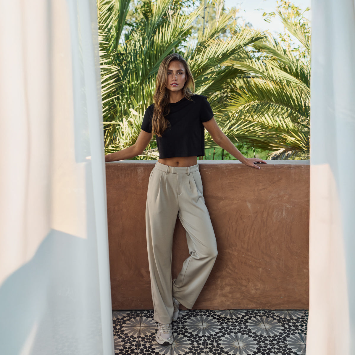 Woman in a black top and light trousers in front of palm trees